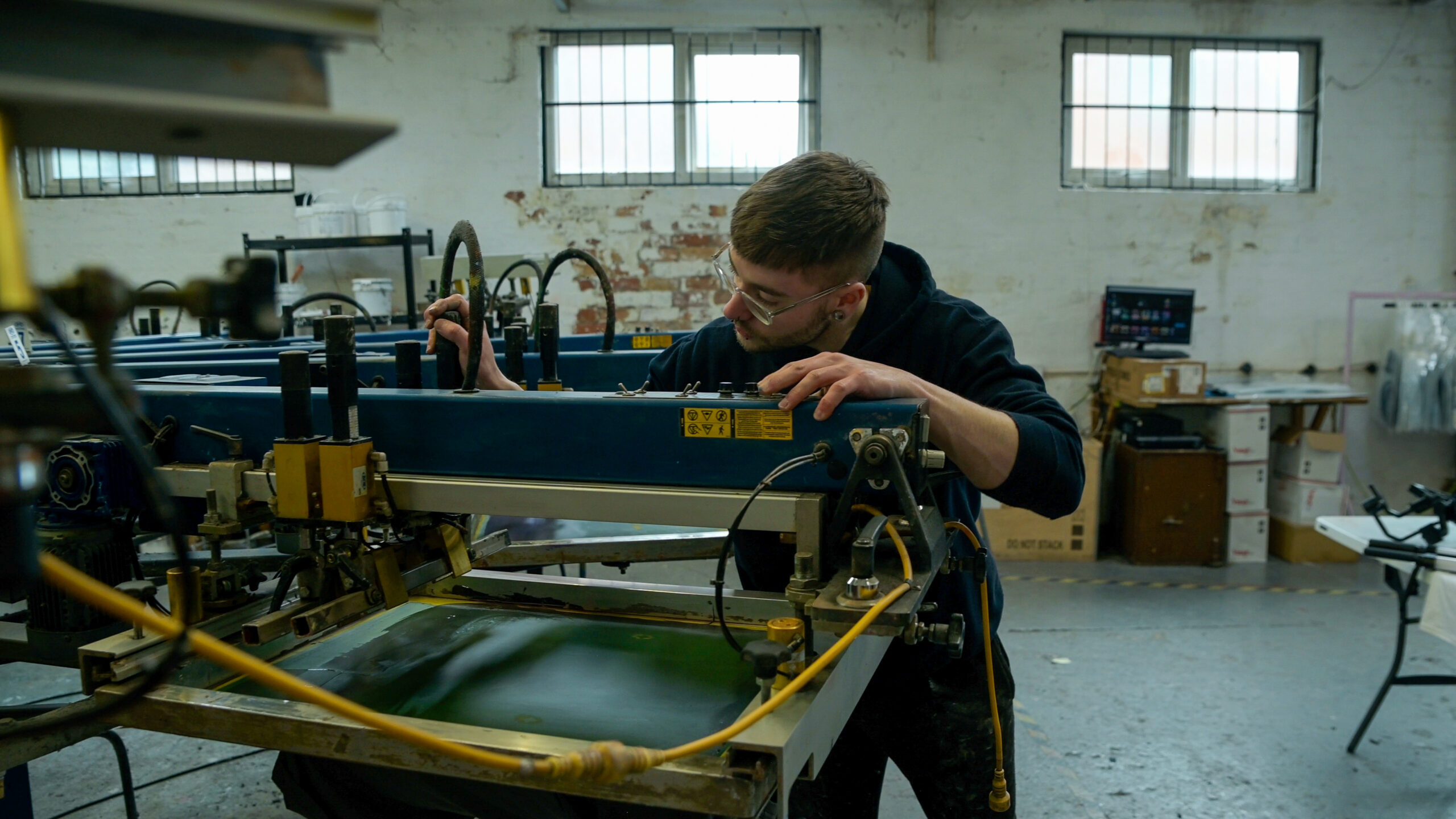 "screen printing technician working on an automated print press to set up a bulk order design"