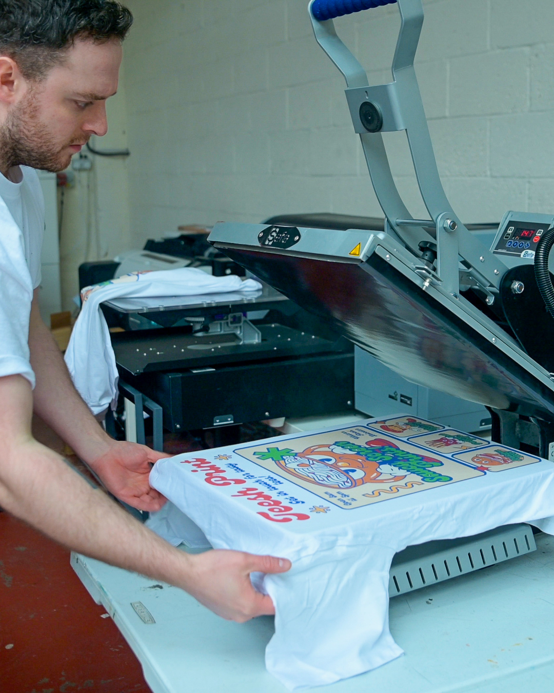 A staff member at teesh print ltd taking off a freshly printed t-shirt from the heat press after dtg printing