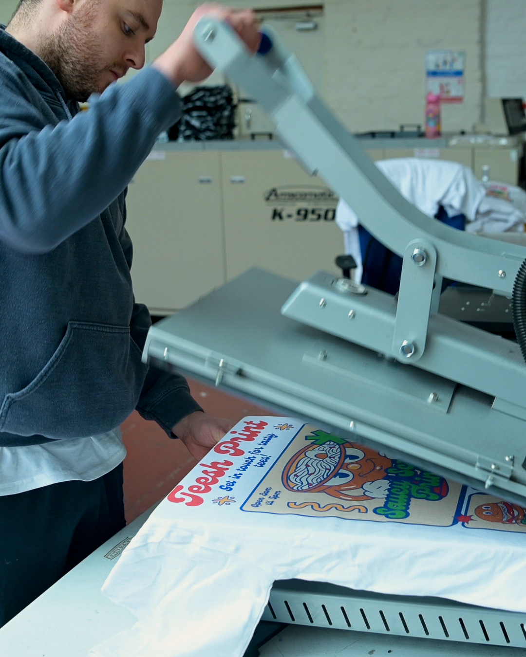 a man using a heat press to print a colourful cartoon design onto a white t shirt.