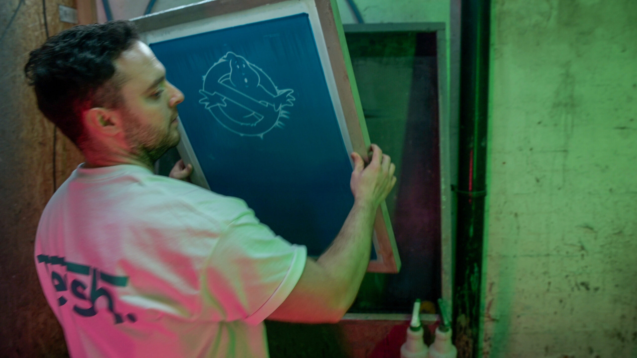 a man taking a screen from a jet washing area for screen printing clothing preparation.