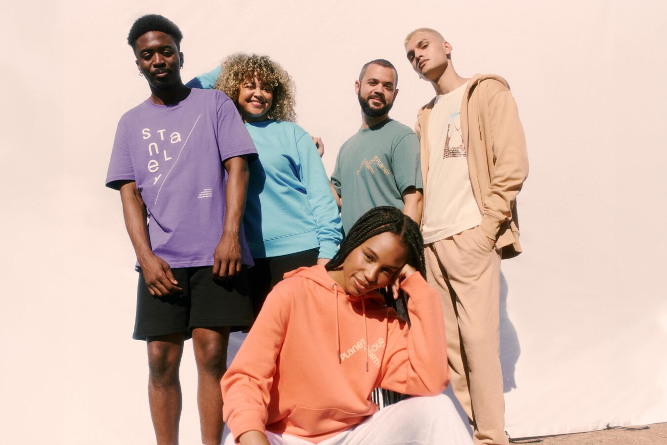 a group of people stood and one person crouched posing in multi coloured garments such as t shirts and hoodies