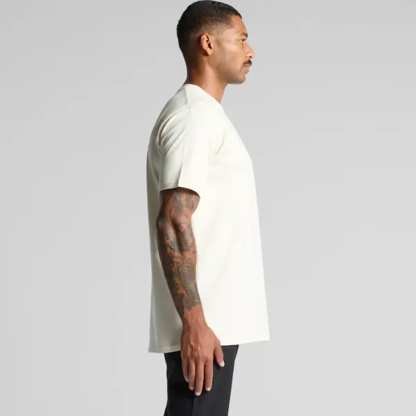 A person wearing the AS Colour 5026 Classic Tee in natural colour, regular fit, standing sideways to showcase the plain front design.