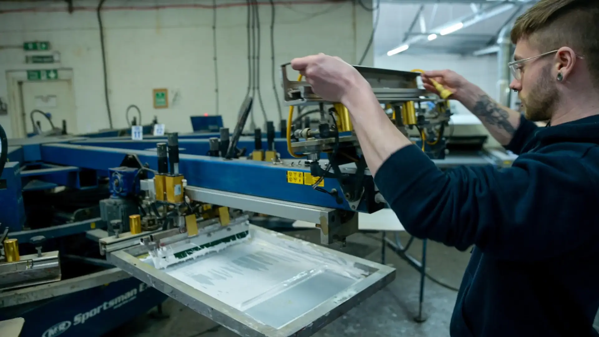 A person operating an automated screen printing rotary machine, setting up a t-shirt printing job.