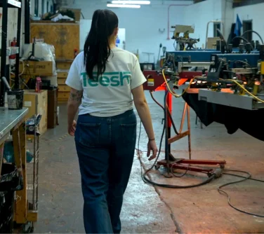 a woman walking around a clothing printing warehouse, wearing a white t shirt as printed uniform with 