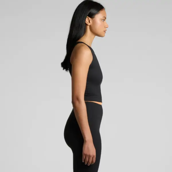Side profile of woman in black workout crop tank and high-waisted leggings on neutral backdrop