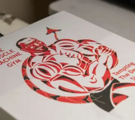 A digital printing design on a white t shirt of a devil with text that reads "muscle machine gym. tempting the devil since 1890"