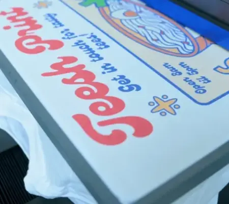 A white t-shirt loaded onto a DTG printer with a cartoon-style design printed onto it.