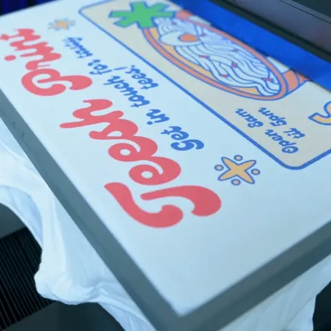 A white t-shirt loaded onto a DTG printer with a cartoon-style design printed onto it.